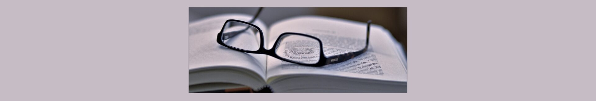 Understanding Online Bookkeeping Terminology A Glossary For Beginners. Gray background, a black box with a open book, pair of black framed glassed laying on the arms.